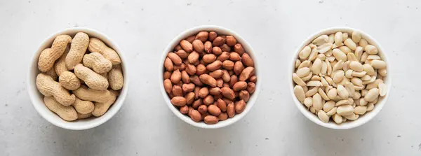 stock image Whole and peeled with blanched and salted peanut nuts in bowls on light background.