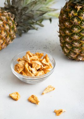 Kavrulmuş ananas parçaları cam kasede hafif arka planda olgun ananas meyveleriyle birlikte. Makro.