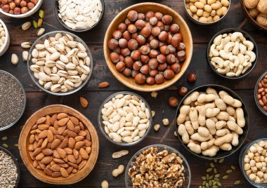 Fıstık, fındık, ceviz, badem, şam fıstığı, ayçiçeği, balkabağı, fındık, fındık ve fındık karışık sağlıklı fındık ve tohumlar çeşitli kaselerde karanlık mutfak masasında..