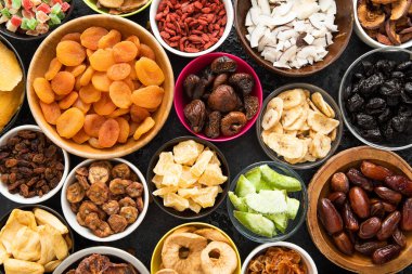 Çeşitli organik sağlıklı kurutulmuş tatlı böğürtlen ve meyveli aperatif siyah arka planda çeşitli kase tabakları.