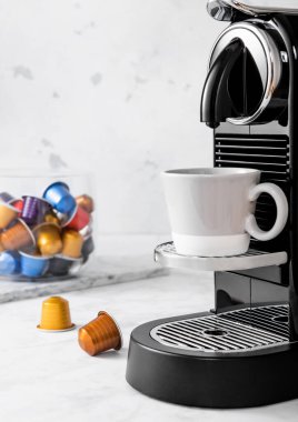 Kahve makinesi, kahve fincanı ve açık mutfak arka planında kahve kapsülleri..