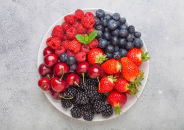 Taze organik yaz meyveleri arka planda beyaz tabakta karıştırılır. Ahududu, çilek, yabanmersini, böğürtlen ve kiraz. Üst görünüm