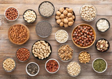 Fıstık, fındık, ceviz, badem, fıstık, fıstık, ayçiçeği, balkabağı, chia, ceviz ve kaju karışımı sağlıklı fındık ve tohumlar ahşap arka planda çeşitli kaselerde.