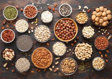 Karışık fındık ve tohumlar çeşitli kaselerde koyu ahşap masa üzerinde. Fıstık, fındık, ceviz, badem, şam fıstığı, ayçiçeği, balkabağı, chia ve kaju..