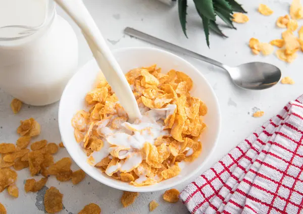 Süt, tabağa dökülüyor. Orijinal sarı mısır gevreği, kahvaltı gevreği, masada kaşık..