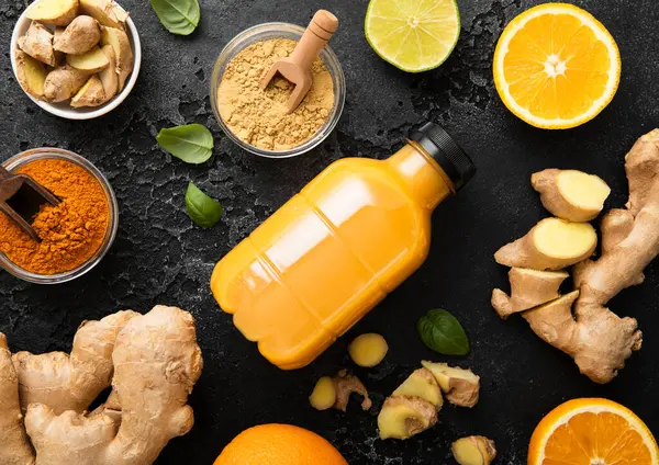 Zencefil ve turuncu enerji içeceği. Siyah mutfak arka planında zencefil kökü ve zerdeçal tozu var..