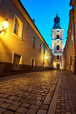 Geceleyin Poznan 'daki barok tarihi kilisesinin kaldırımlı caddesi ve çan kulesi.
