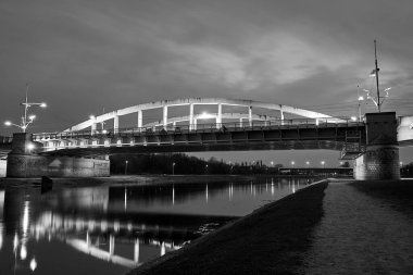 Polonya 'nın Poznan şehrinde gece boyunca Warta Nehri üzerindeki yol köprüsünün çelik yapısı, tek renkli.