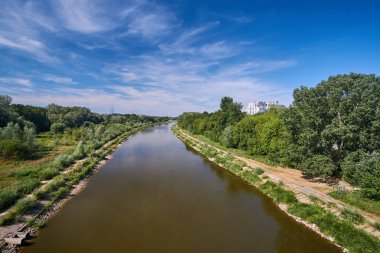 Landscape with trees, meadows, and multi-story residential buildings on the Warta River during summer, Poland