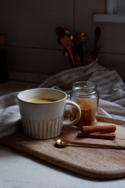 Altın latte, bir fincan sıcak zerdeçal latte ve tahtanın üzerinde tarçın çubukları.