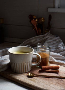 Altın latte, bir fincan sıcak zerdeçal latte ve tahtanın üzerinde tarçın çubukları.