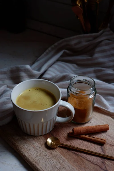 golden latte, cup of hot turmeric latte with cinnamon sticks on wooden cutting board