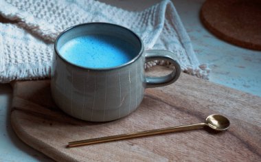 Seramik bardakta mavi spirulina latte ve tahta kesim tahtası arka planında kaşık.