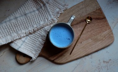 Seramik bardakta mavi spirulina latte ve tahta kesim tahtası arka planında kaşık.