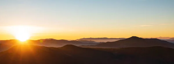 Mountain sunrise header. Mountain silhouettes and rays of the rising sun