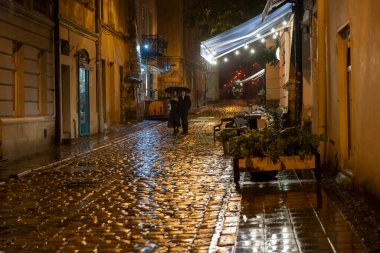2020-09-29 Lviv, Ukraine. Rainy night on the old lviv city streets. A pair with umbrella goes under the pouring rain