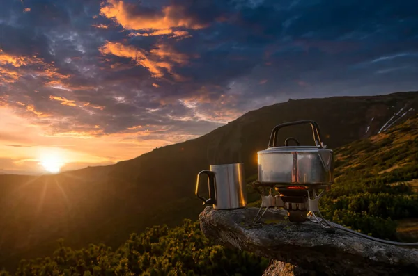 Cup of hot tea on the mountain top. Amazing mountain sunset with tourist stove, boiling teapot and a cup of tea. Symbol of vacation, freedom, outdoor exploration and wanderlust.