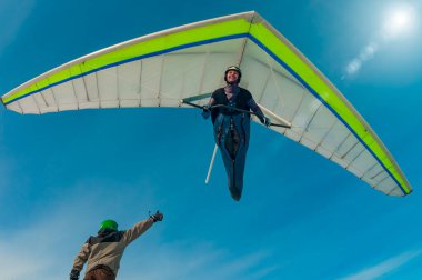 Aerial stunt. Hang glider pilot gives high five to his friend standing on the ground with thumb up. Beauty of extreme sports clipart