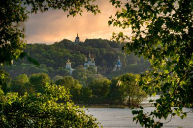 Gün batımında Kyiv şehri manzarası. Kyiv 'deki Dnipro nehrinin sol kıyısında güzel bir manastır.