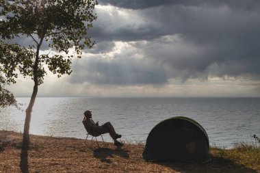 Deniz kıyısında katlanan sandalyede oturan yalnız adam manzaranın tadını çıkarıyor. Sadece meditasyon ve rahatlama. Gezgin şehvet ve vahşi doğada tatil
