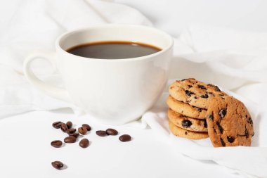 Fasulye ve kurabiyeli beyaz kumaş üzerinde büyük bir fincan sabah kahvesi.