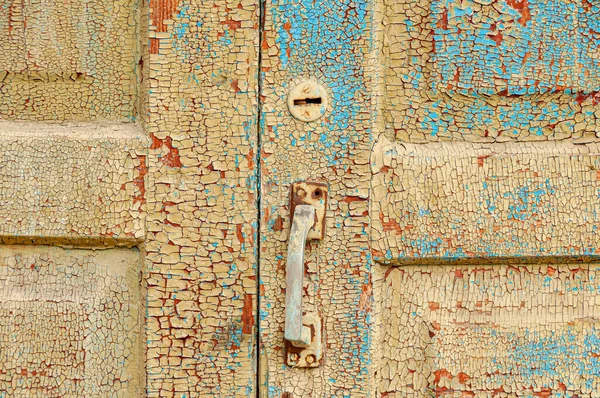 Old rustic wooden door fragment with keyhole and handle and cracked and ripped paint.
