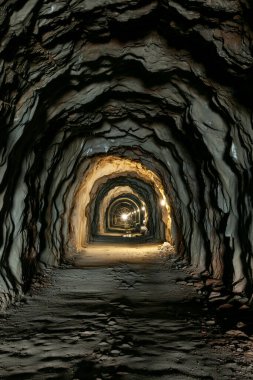 Kayadaki eski karanlık tünel. Tünelin sonunda ışık var. Dikey fotoğraf