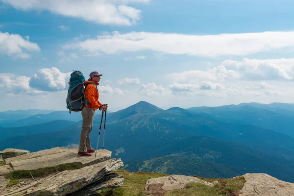 Hiker woman with backpack and trekking poles on the mountain top. Active lifestyle and outdoor vacation in the mountains