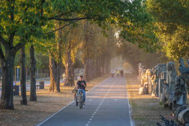 2023-09-10 Kyiv, Ukrayna. Şehir parkında bisiklete binen insanların olduğu bisiklet yolu. Parkta ılık bir sonbahar akşamı