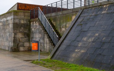 Berlin Şehri Temizlik Servisi 'nin turuncu çöp sepeti gri bir duvarın önünde, Spree nehir kıyısı hükümet bölgesinde, Berlin, Almanya