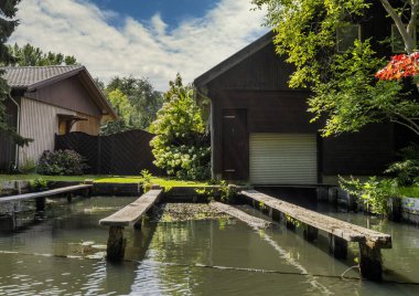 The image depicts a tranquil river landscape, with boats, wooden bridges, and single-family homes along the water. Surrounded by nature and landscape, the scene has a natural and peaceful atmosphere. Lbbenau, Brandenburg, Germany