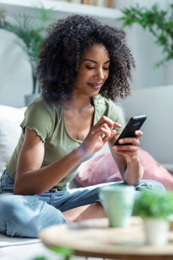 Evdeki kanepede oturup kahve içerken kendine güvenen bir kadının cep telefonunu kullanması..