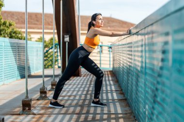 Genç, sportif bir kadının, köprüde gerinirken kulaklıkla müzik dinlemesi..