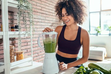 Evdeki mutfakta sebze yeşili smoothie yapan genç bir kadın..