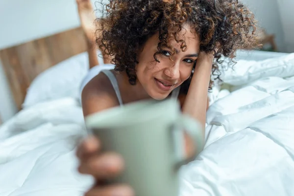 美しいです女性のショットコーヒーを飲みながらカメラを見ながらベッドの上に滞在 — ストック写真