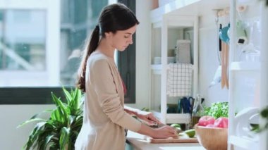 Sağlıklı genç bir kadının taze sebze keserken evdeki mutfakta sağlıklı yemek pişirdiği video..