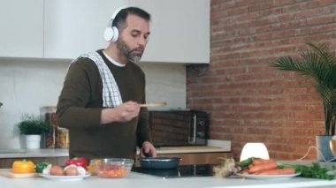 Yakışıklı, olgun bir adamın hazırladığı yemekleri yerken evde kulaklıkla müzik dinlediği bir video..