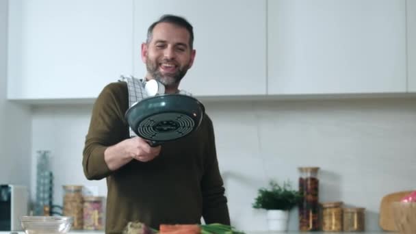 自宅でキッチンで楽しみながら鍋で野菜を炒めハンサムな熟年男性のビデオ — ストック動画
