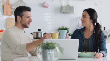 Bu sevimli çiftin, evdeki mutfakta bardaklarını tokuştururken laptoplarını kullanarak yolculuk aramalarını gösteren bir video..