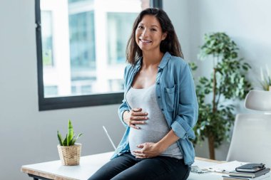 Shot of beautiful pregnant woman relaxing while looking at camera at home clipart