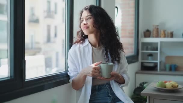 视频中美丽的女人一边喝着一杯咖啡 一边盼望着站在窗边 — 图库视频影像