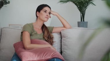 Evdeki oturma odasındaki kanepede oturmuş sorunları düşünen endişeli bir kadının videosu..