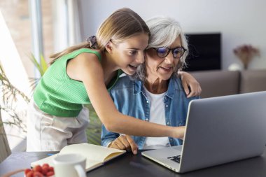 Shot of happy granmother using laptop with her granddaughter at home.
