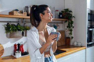 Shot of beautiful young woman drinking coffee while standing in the kitchen at morning