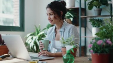 Serada dizüstü bilgisayarıyla çalışırken bir fincan kahve içen gülümseyen kadının videosu..