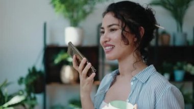 Gülümseyen kadının serada cep telefonunu kullanırken bir fincan kahve içtiği video..