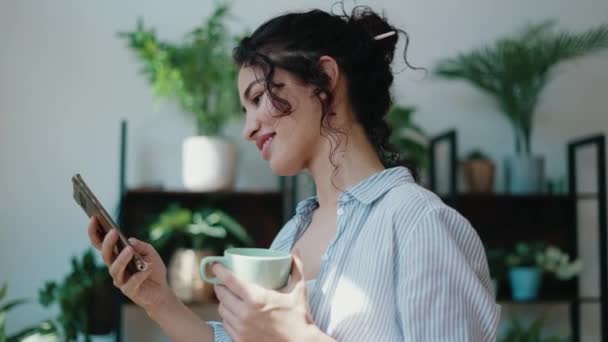 Βίντεο Χαμογελαστή Γυναίκα Πίνοντας Ένα Φλιτζάνι Καφέ Ενώ Χρησιμοποιώντας Κινητό — Αρχείο Βίντεο