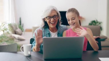 Video of cute granddaughter with grandmother waving hand during video call using laptop at home.