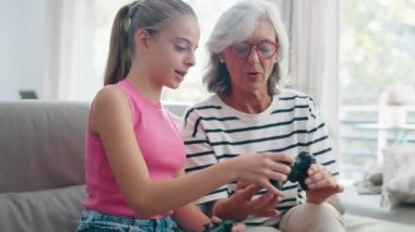 Video of cute granddaughter teaching her grandmother to play video games on the console on sofa at home
