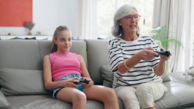 Video of cute granddaughter teaching her grandmother to play video games on the console on sofa at home